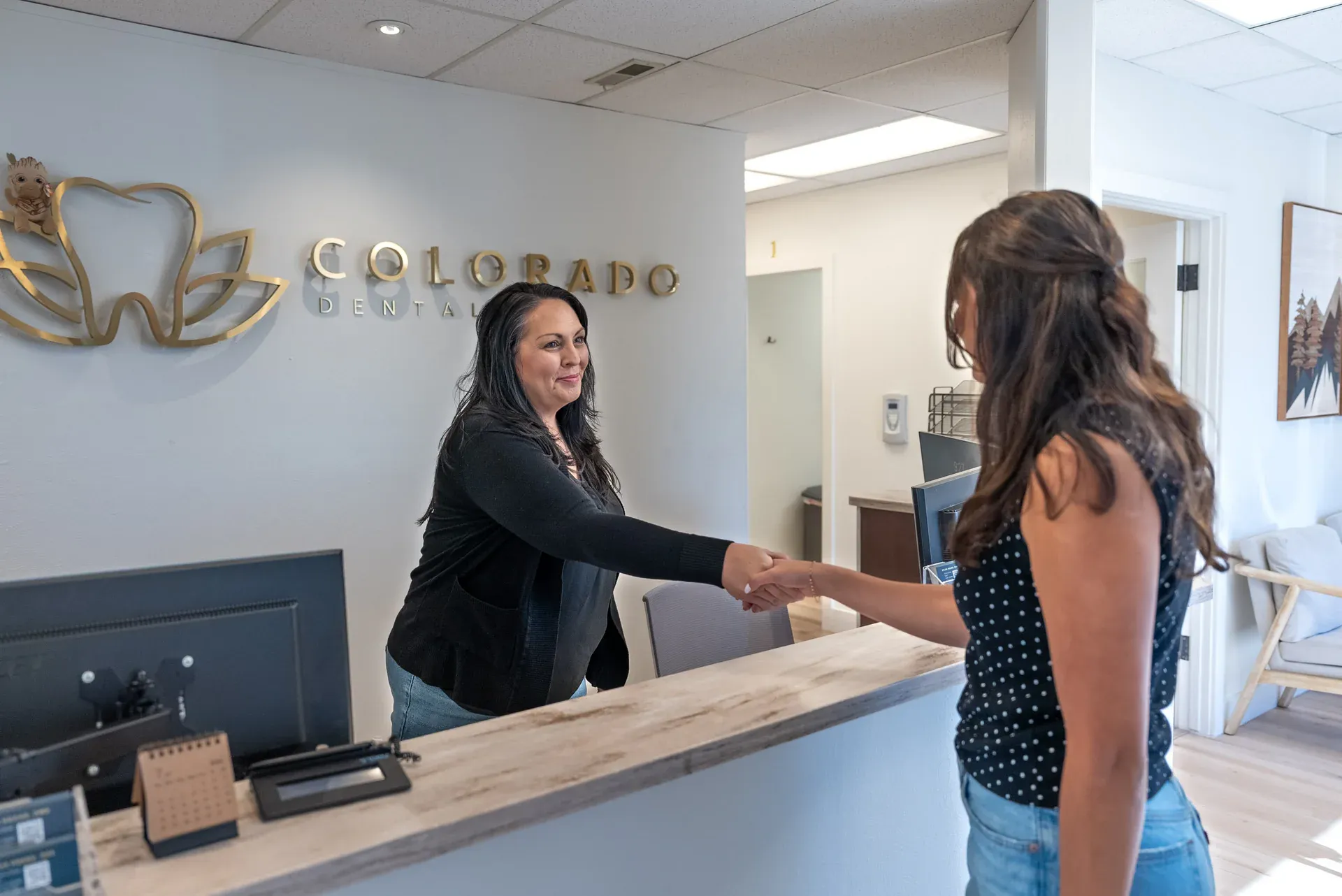 A patient being welcomed at the Colorado Dental Spa reception desk beneath the practice logo in Golden, CO